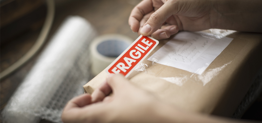 Unas manos sosteniendo una pegatina de "frágil" al embalar